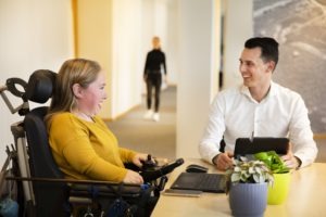 Twee mensen aan een Tafel. Een vrouw in een rolstoel en een man achter een laptop