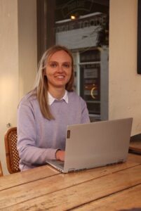 jonge vrouw met lang blond haar aan een tafel achter een laptop