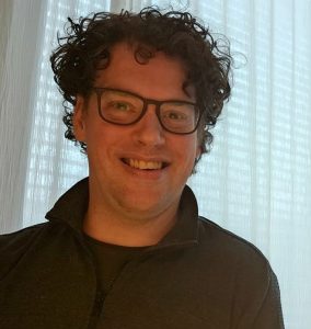 Man met donkerbruine krullen en een bril.